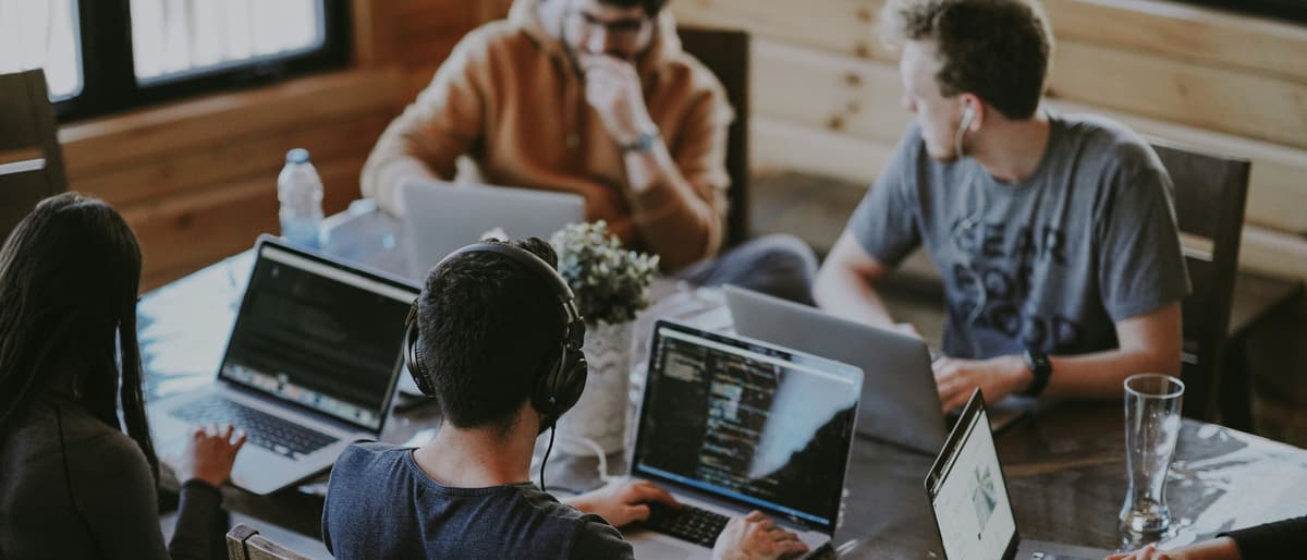 Software developers collaborating at a table, writing code on laptops